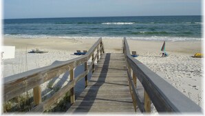 A wooden boardwalk leading to a sandy beach with a few beach chairs and umbrellas.