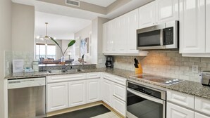 A modern kitchen with white cabinetry, granite countertops, a built-in microwave, and a dishwasher.