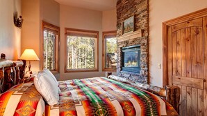 Un dormitorio con chimenea de piedra, ventanas grandes, una cama con manta colorida y una puerta de madera.