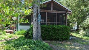 A cabin with a large window, surrounded by dense greenery and a wooden deck. - Walk to Private Beach, Great screened porch, Chefs kitchen, Open beam design (Union Pier)