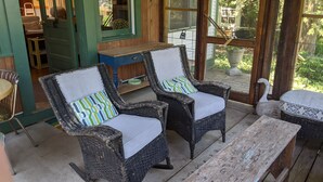 A porch with wicker rocking chairs, a wooden table, and a view of a house through a screened door. - Walk to Private Beach, Great screened porch, Chefs kitchen, Open beam design (Union Pier)