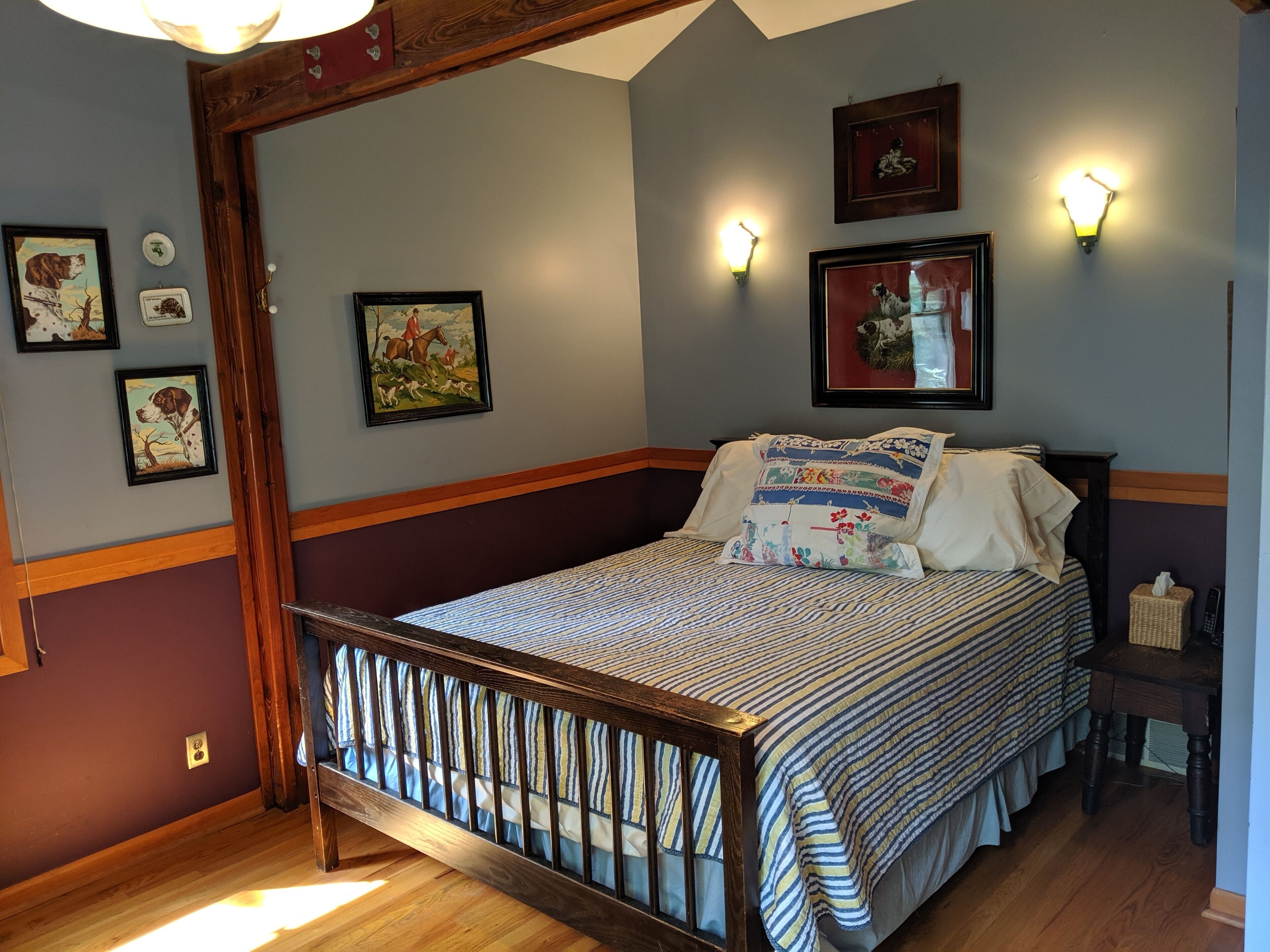 Ein Schlafzimmer mit einem hölzernen Himmelbett, Holzboden und einer Wand mit gerahmten Bildern und Wandleuchten.