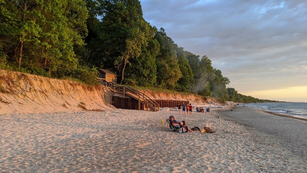 Una spiaggia sabbiosa con una scala di legno che conduce a un edificio, circondata da alberi.