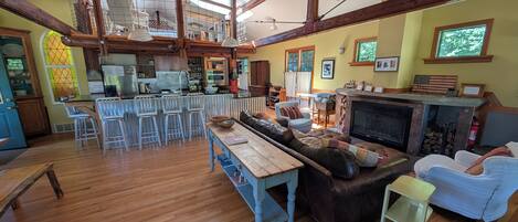 A spacious living area with a fireplace, a dining table, and a kitchen in the background.