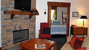 A living room with a stone fireplace, a television mounted on the wall, a red armchair, a wooden coffee table, and a sofa with red cushions. - Timber Ridge Cabin Apartment, Forested Retreat Close to Natchez Trace, Franklin! (Franklin)