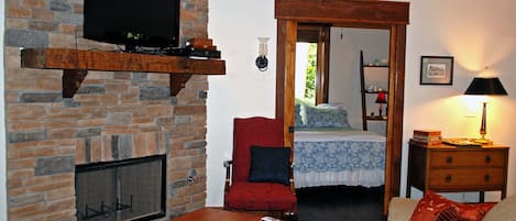 Un salon avec une cheminée en pierre, un téléviseur fixé au mur, un fauteuil rouge, une table basse en bois et un canapé avec des coussins rouges.