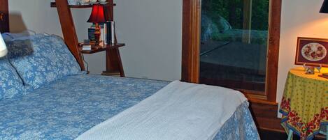 A bedroom with a large bed, a wooden ladder, a window, and a small table with a lamp.