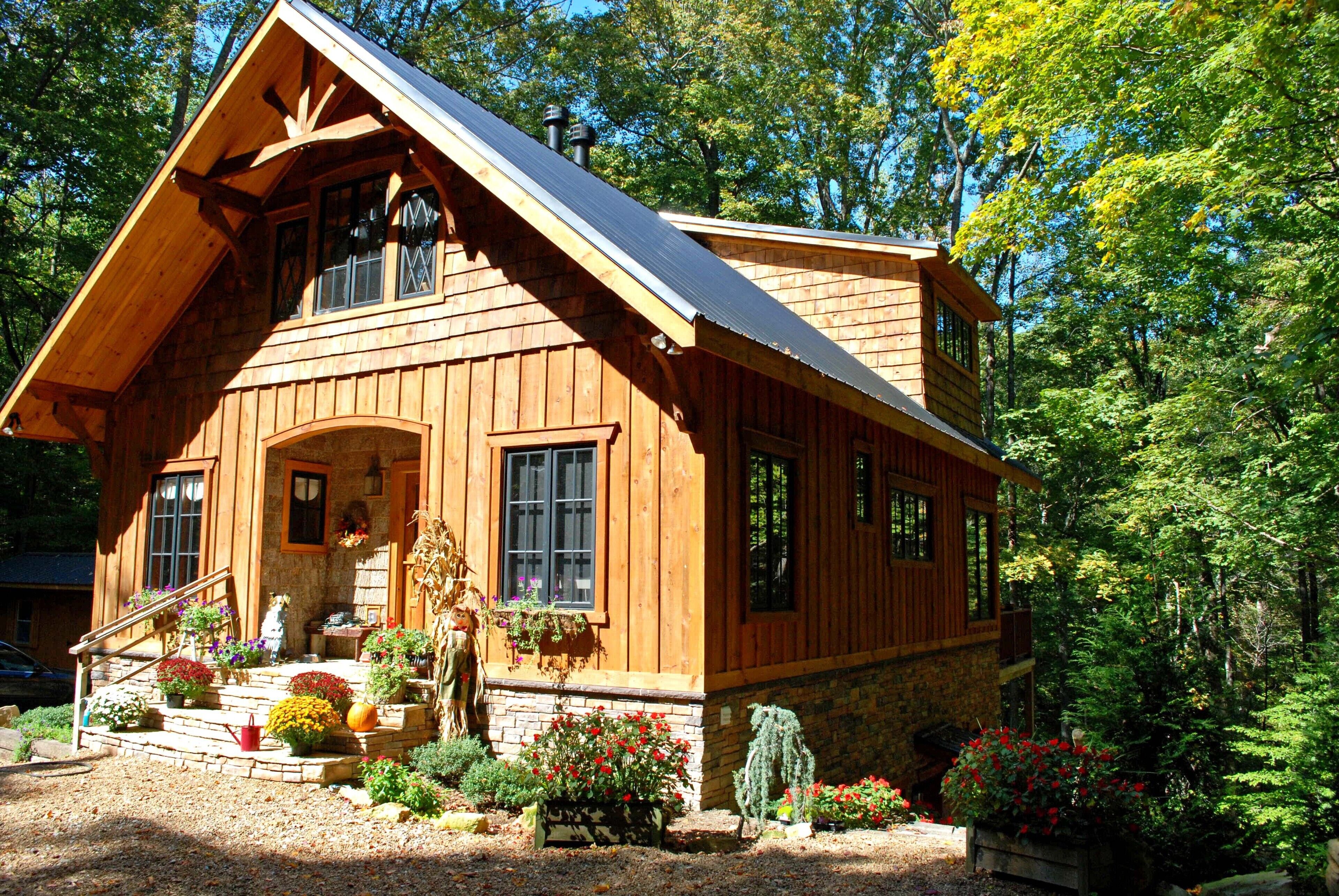 A wooden cabin with a sloped roof, a front porch with steps, and a garden with various plants and flowers.