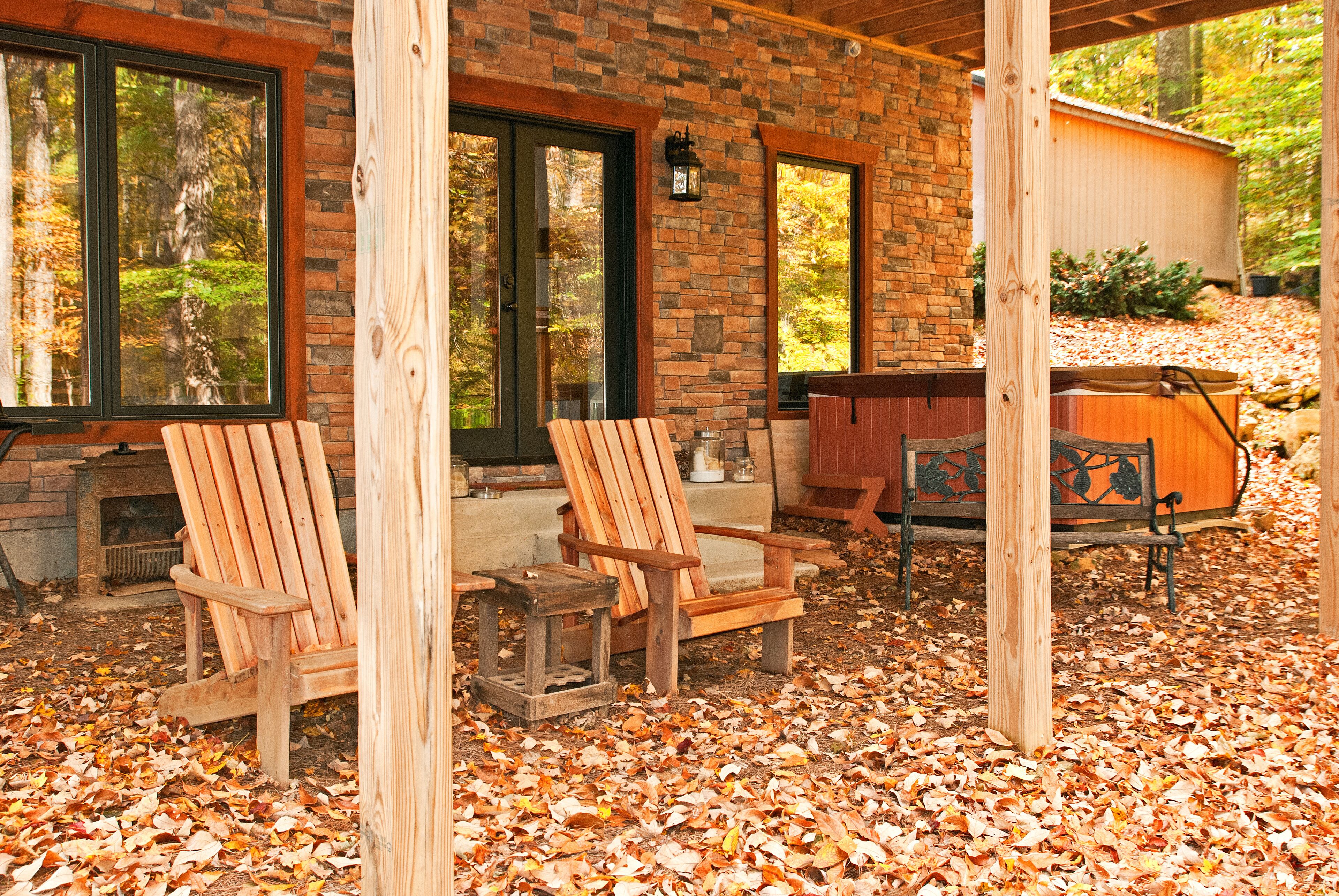 A covered patio area with two wooden Adirondack chairs, a stone fireplace, and a wooden deck.