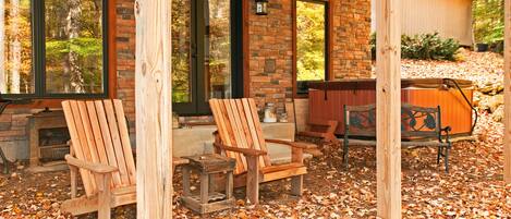 A covered patio area with two wooden Adirondack chairs, a stone fireplace, and a wooden deck.