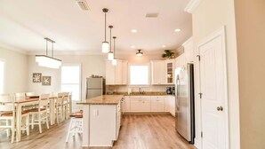 Une cuisine moderne avec des meubles blancs, un îlot central et des luminaires suspendus.
