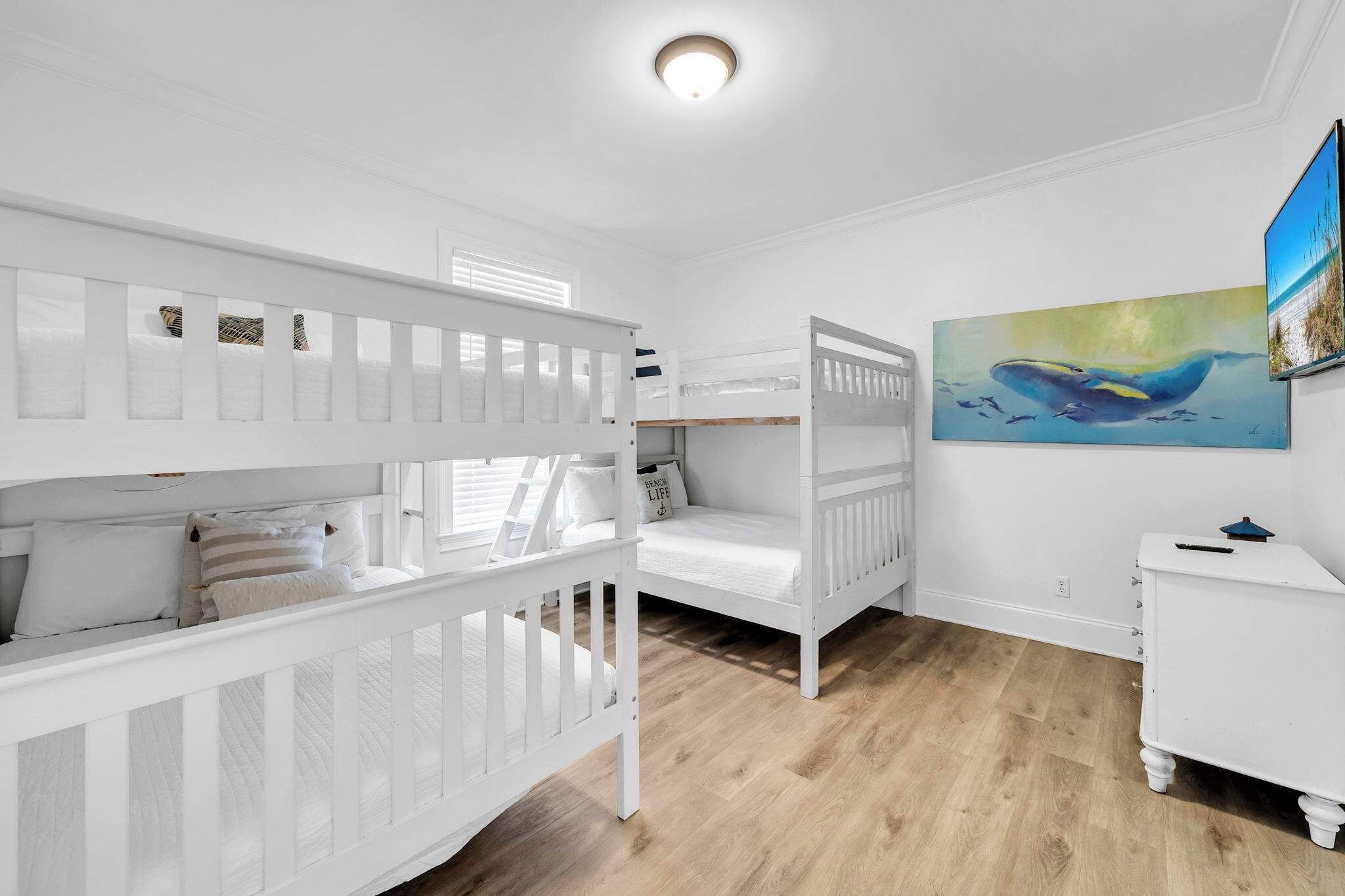 Ett rum med våningssängar, en tavla och en liten vit byrå.