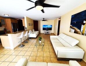 A modern living room with a sofa, chairs, a TV, and a ceiling fan.