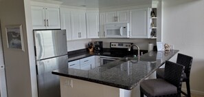 A kitchen with white cabinets, a stainless steel refrigerator, a microwave, a stove, and a granite countertop.