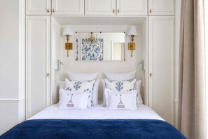 A bedroom with a bed, white walls, a chandelier, and a mirror above the bed.