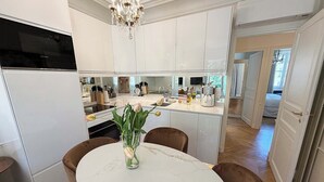 A modern kitchen with white cabinetry, a marble dining table, and a chandelier. - Spacious, Enchanting 1 Bedroom + Balcony and Insta-worthy Eiffel View (Paris)