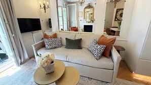 A living room with a sofa, two side tables, a flat-screen TV, a chandelier, and large mirrors. - Spacious, Enchanting 1 Bedroom + Balcony and Insta-worthy Eiffel View (Paris)
