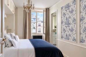 A bedroom with a bed, a window, a radiator, and a door leading to a bathroom. - Spacious, Enchanting 1 Bedroom + Balcony and Insta-worthy Eiffel View (Paris)