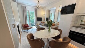 A dining area with a round table, four chairs, a vase with flowers, and a view of the outdoors through large windows. - Spacious, Enchanting 1 Bedroom + Balcony and Insta-worthy Eiffel View (Paris)
