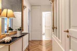 A hallway with a mirror, a lamp, a potted plant, and a door with a brass handle. - Spacious, Enchanting 1 Bedroom + Balcony and Insta-worthy Eiffel View (Paris)