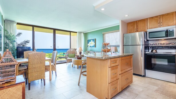A kitchen with wooden cabinets, stainless steel appliances, and a view of the ocean. -  Beachfront ,Ground floor, Sugar Beach, Corner  unit 114 - Steps to the Ocean!!! (Kihei)