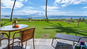 A patio with a round table and wicker chairs, overlooking a grassy area and the ocean. -  Beachfront ,Ground floor, Sugar Beach, Corner  unit 114 - Steps to the Ocean!!! (Kihei)