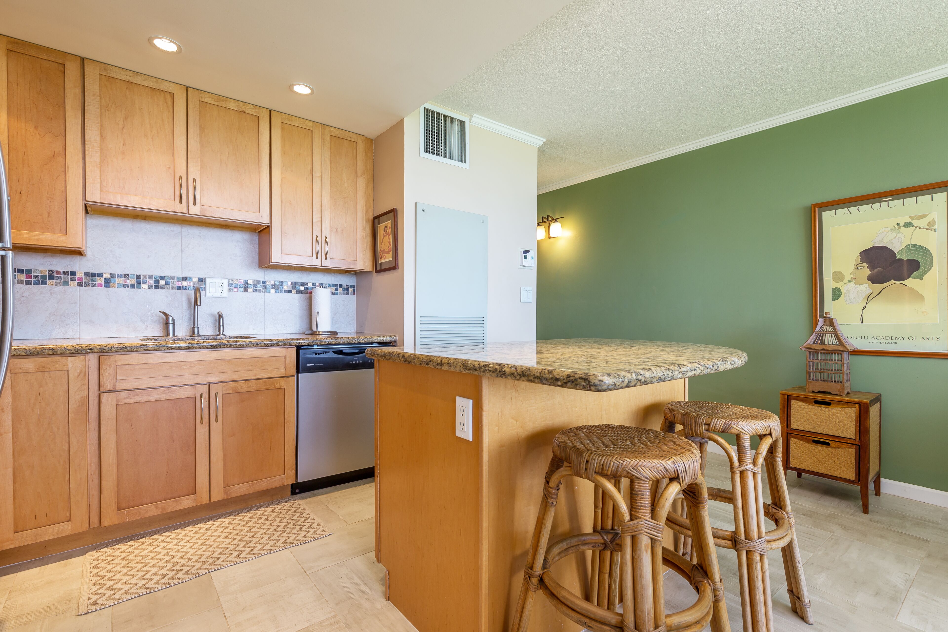 A kitchen with wooden cabinets, a built-in dishwasher, a granite countertop, and a small island with bar stools.