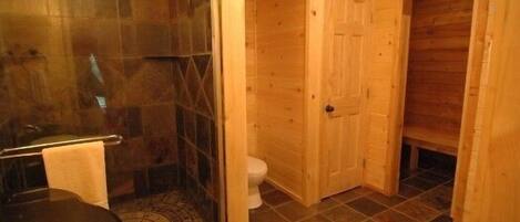 Un baño de madera con cabina de ducha de vidrio, un inodoro y una puerta de madera.