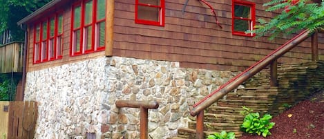 Una cabaña con cimientos de piedra, ventanas de marco rojo y fachada de madera.