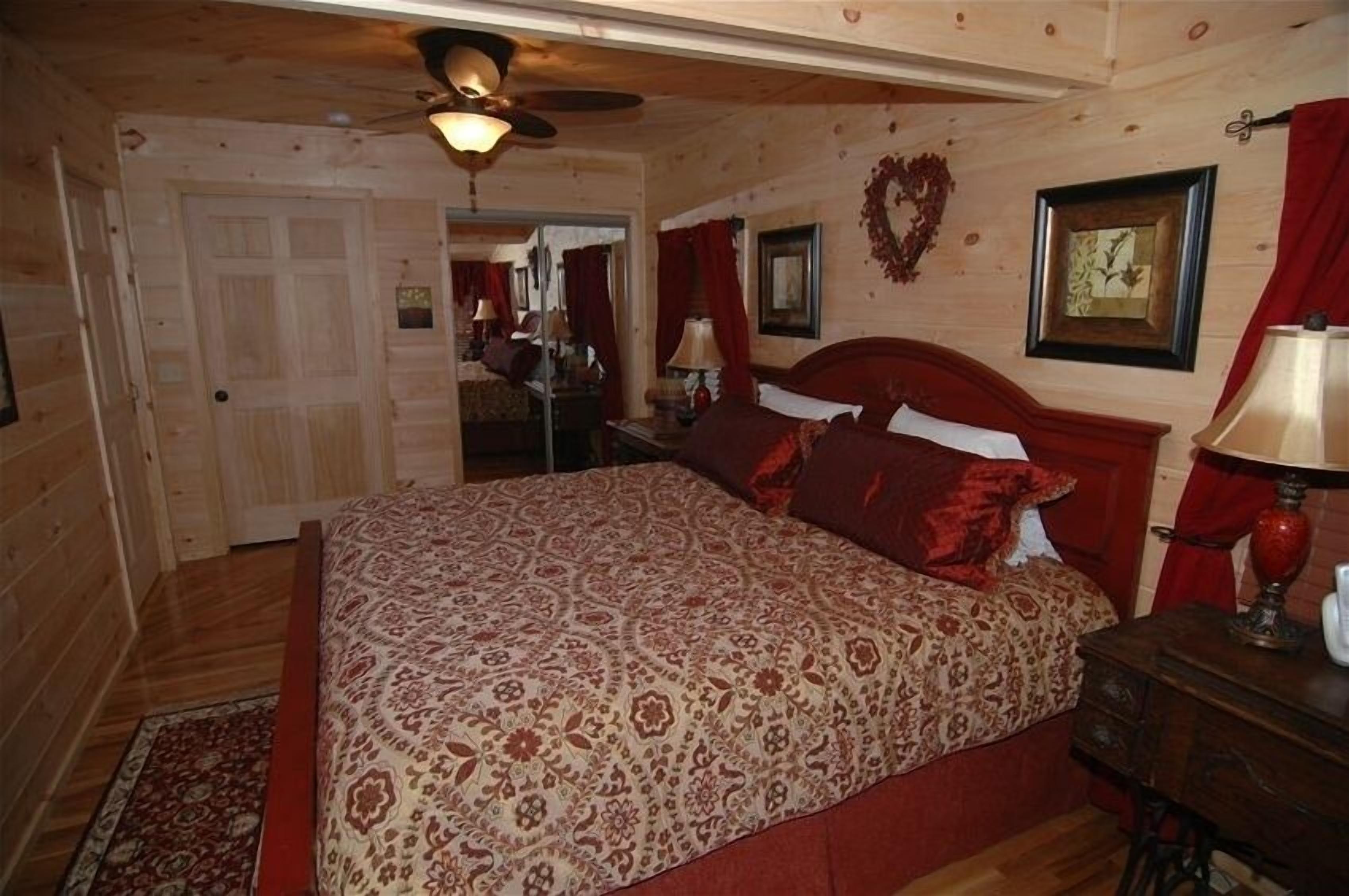 A wooden-paneled bedroom with a bed, a nightstand, a mirror, and a ceiling fan.
