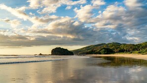 Ein Strand mit einem Felsen, ruhigem Wasser und klarem Himmel.