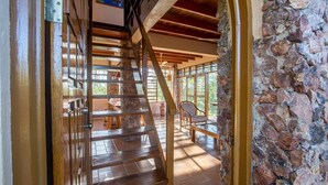 Eine Holztreppe führt zu einem Zimmer mit Steinwänden und Blick ins Freie.