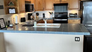 A modern kitchen with wooden cabinets, a stainless steel refrigerator, a built-in oven, and a large island with a sink. - Orcas-Beautiful Modern Home- Large New Deck- Water View- Privacy- Dog Friendly (Rosario)