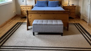 A bedroom with a wooden bed, two nightstands, a bench, a window, and a framed picture on the wall. - Orcas-Beautiful Modern Home- Large New Deck- Water View- Privacy- Dog Friendly (Rosario)