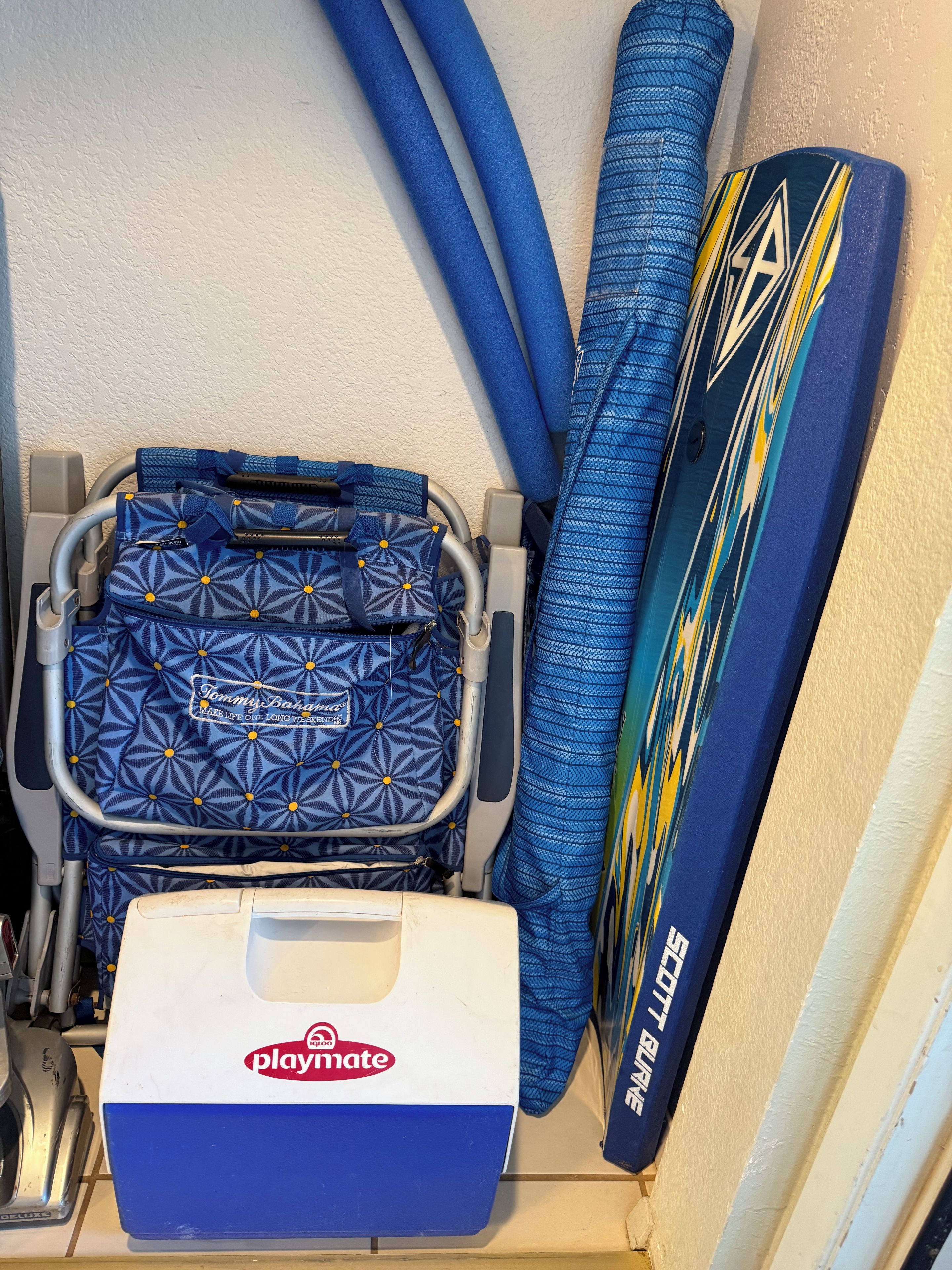 A storage unit with a blue patterned bag, a blue and yellow board, and a Playmate cooler.