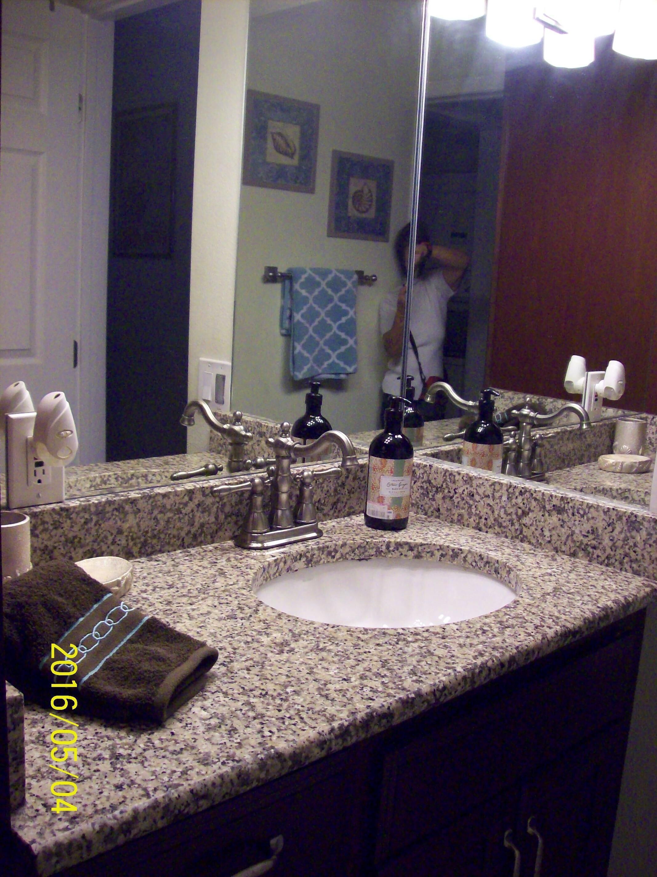 Un baño con encimera de granito, lavamanos, espejo y perchero.
