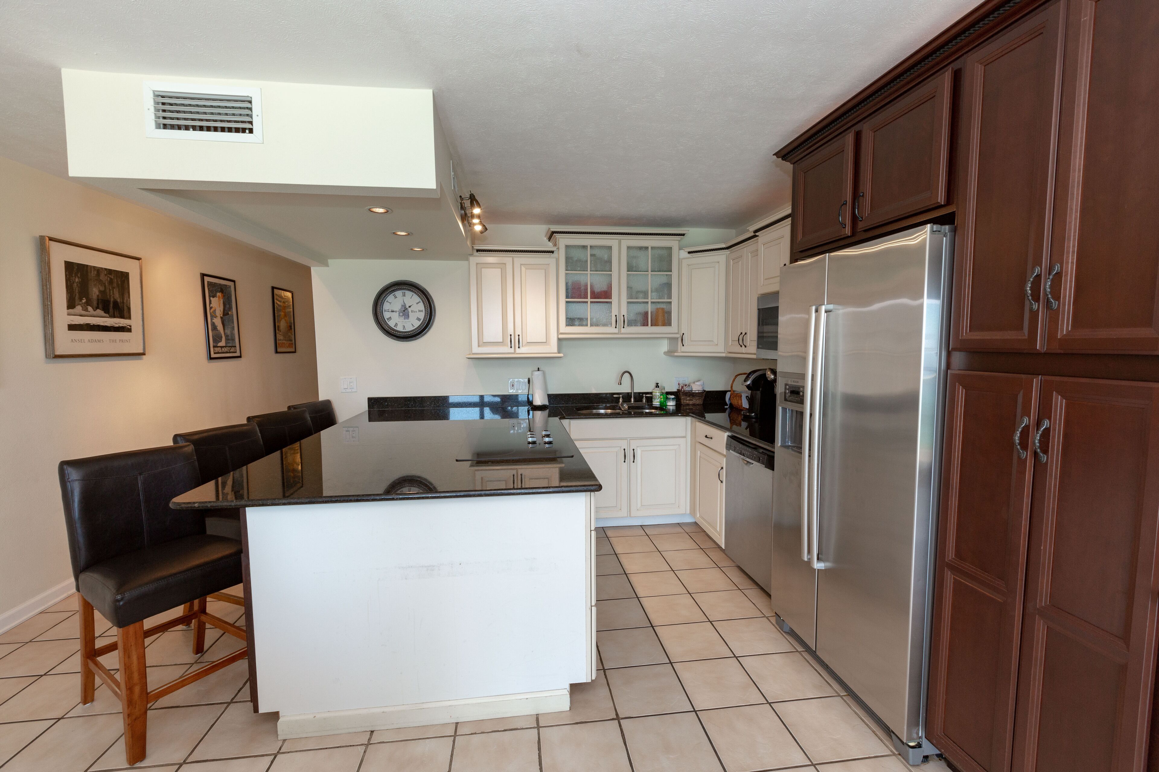 A modern kitchen with a central island, wooden bar stools, white cabinetry, and stainless steel appliances.