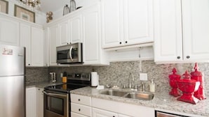 A kitchen with white cabinets, stainless steel appliances, granite countertops, and a red decorative item on the counter. - Absolutely Awesome, the Captain's Cottage (Savannah)