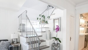 Eine Treppe mit Metallgeländer führt zu einer erhöhten Ebene, ein graues Sofa mit Kissen, ein kleiner Tisch mit Lampe und ein Blumentopf.