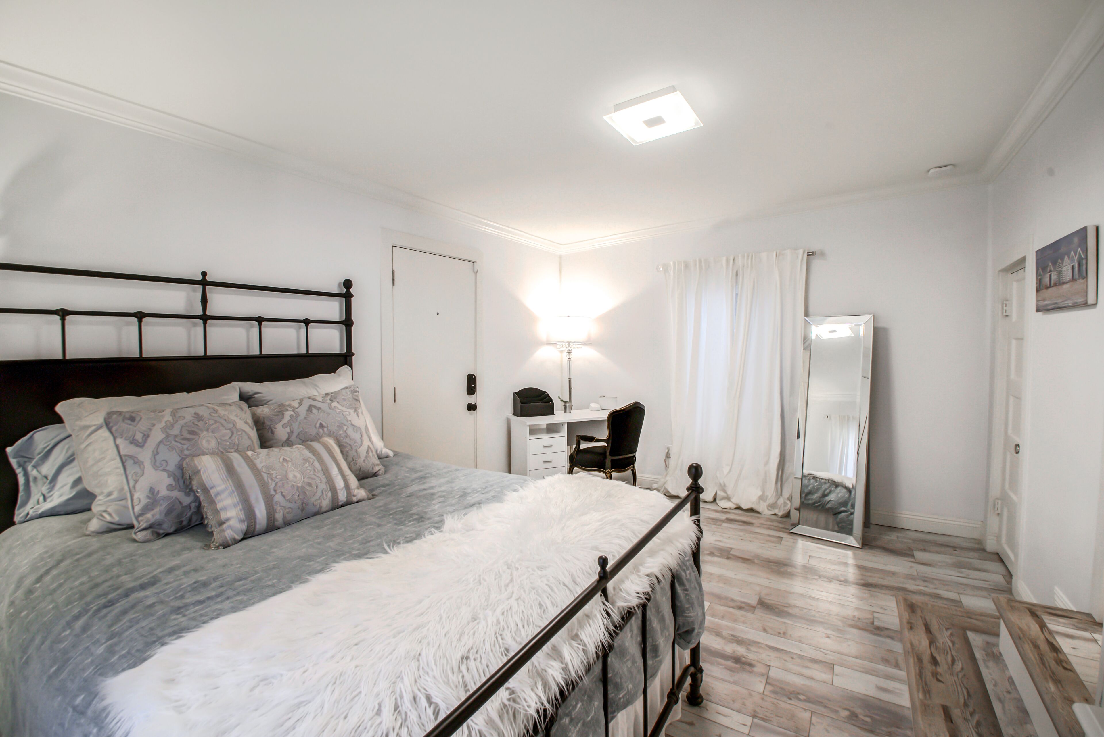 Um quarto com uma cama, uma escrivaninha, uma cadeira, um espelho e um guarda-roupa.