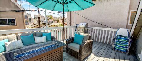 A deck with a glass-top table, wicker furniture, and a grill.