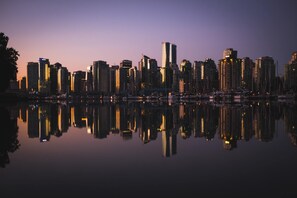 A city skyline at dusk with buildings reflecting on a calm body of water.