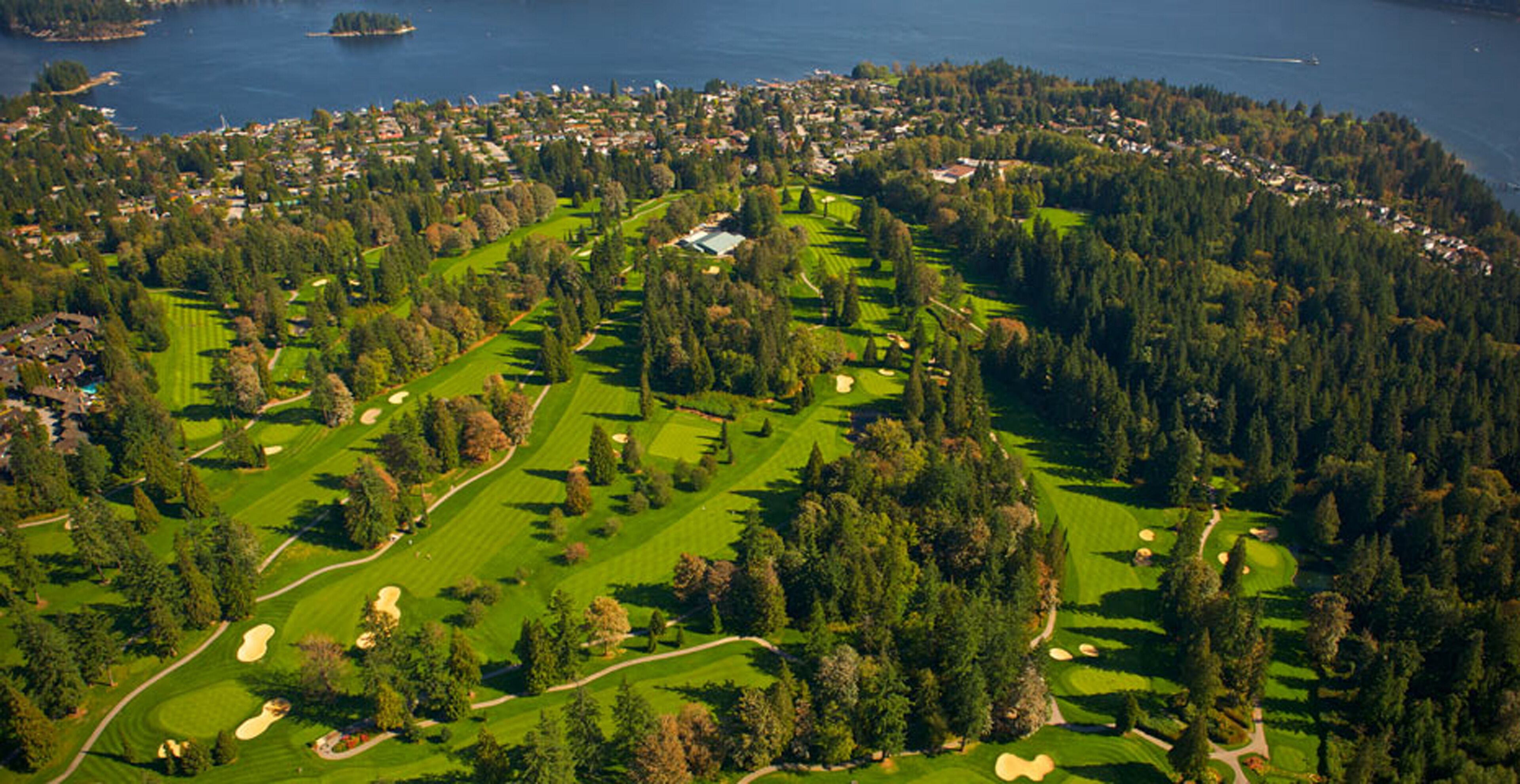 Ein Golfplatz mit mehreren Spielbahnen und Sandbunkern, umgeben von dichtem Wald und Wohngebieten.