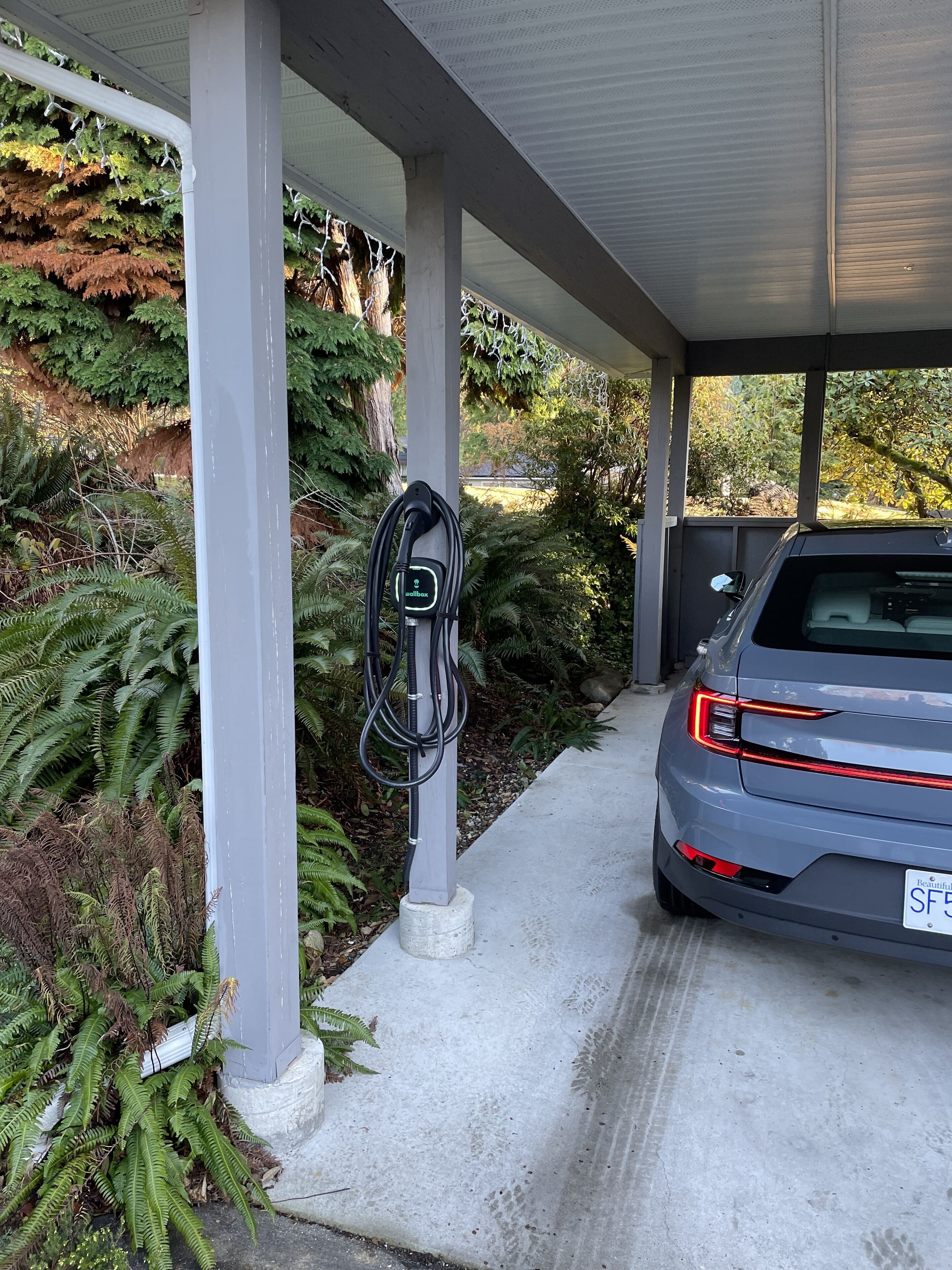 A parking area with a charging station and a car parked under a covered structure.