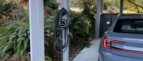 A parking area with a charging station and a car parked under a covered structure.