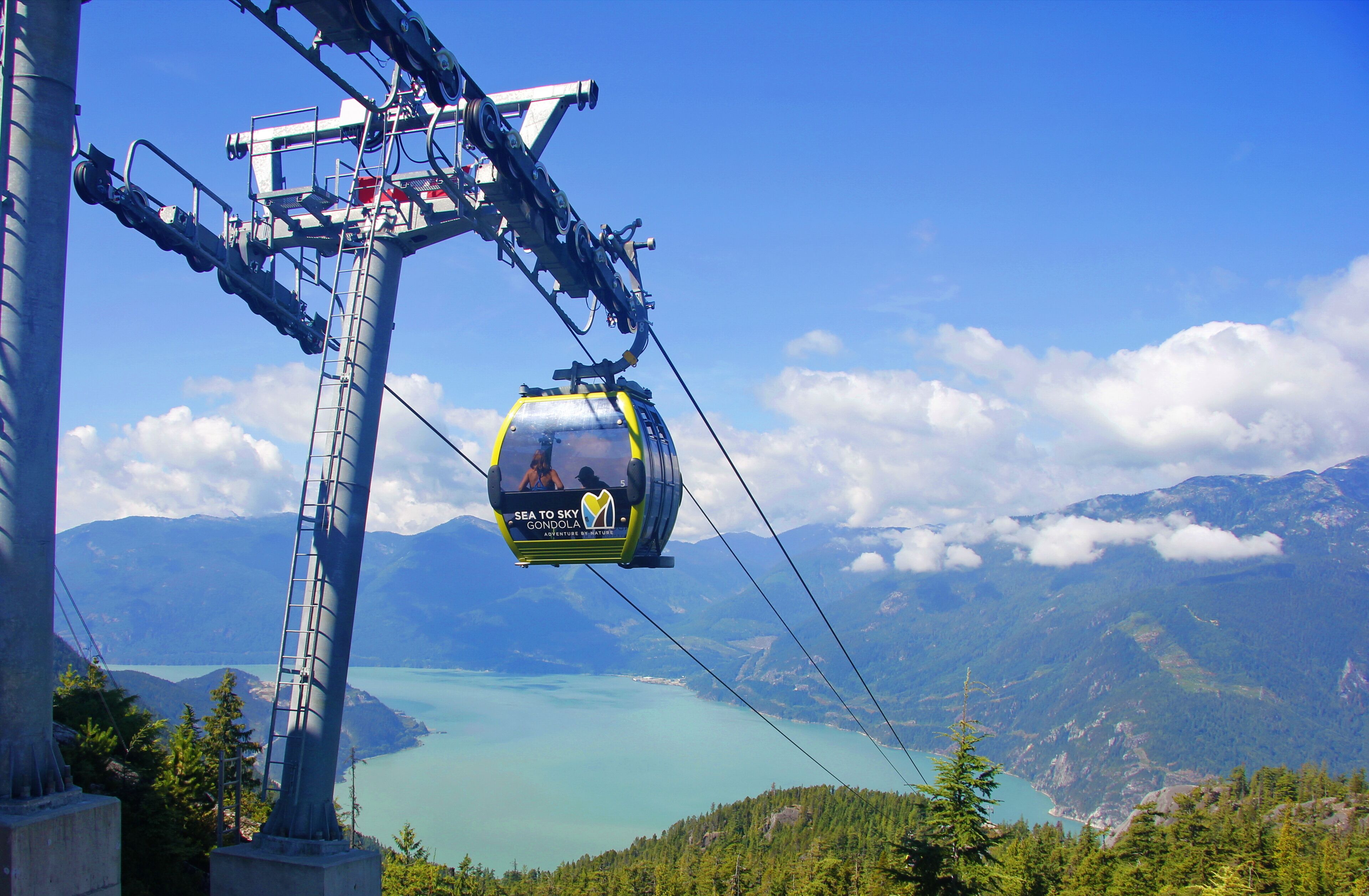 Eine Seilbahn mit Fahrgästen, einem Berg im Hintergrund und einem See.