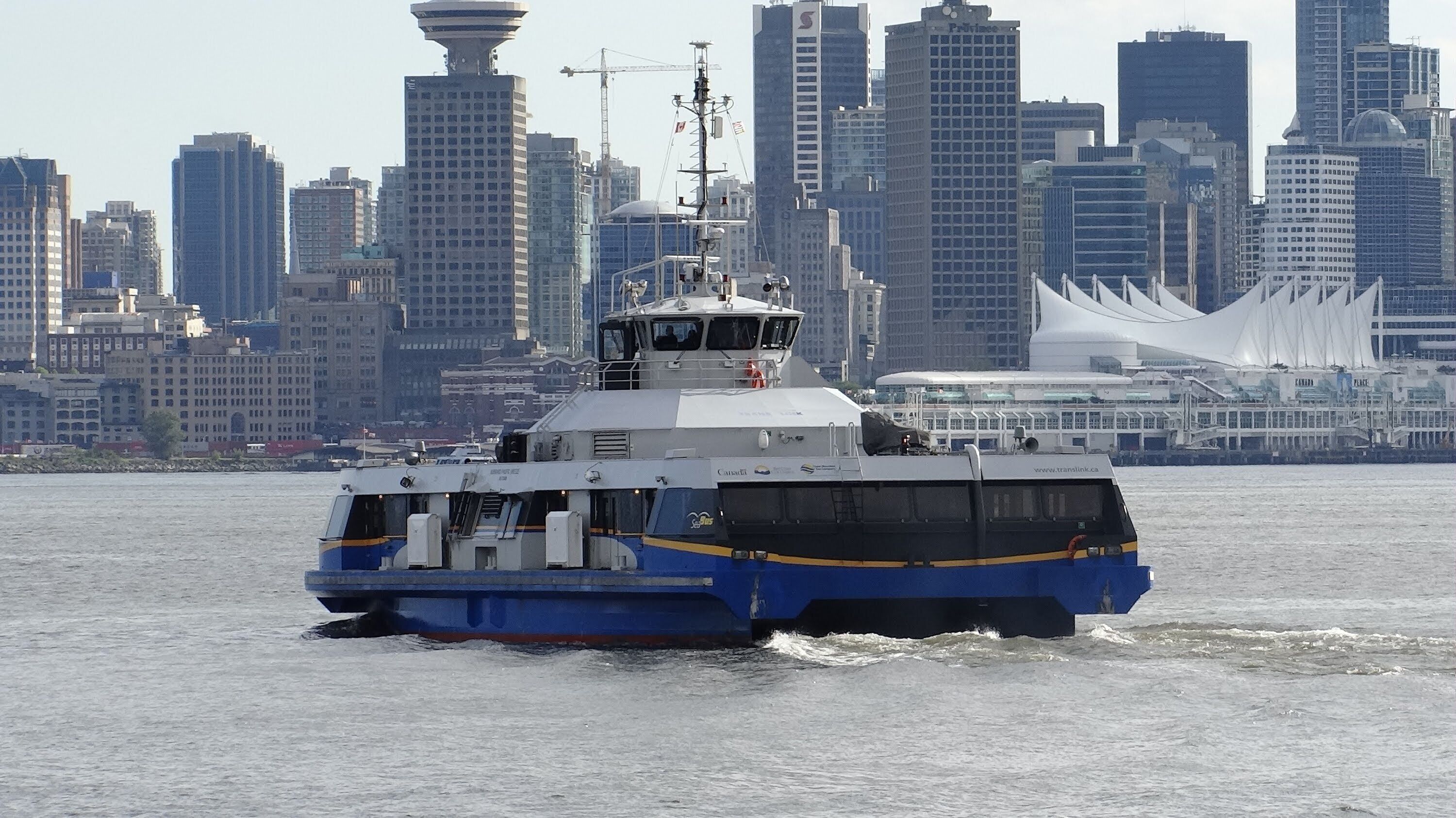 A ferry moving through a body of water with a city skyline in the background.