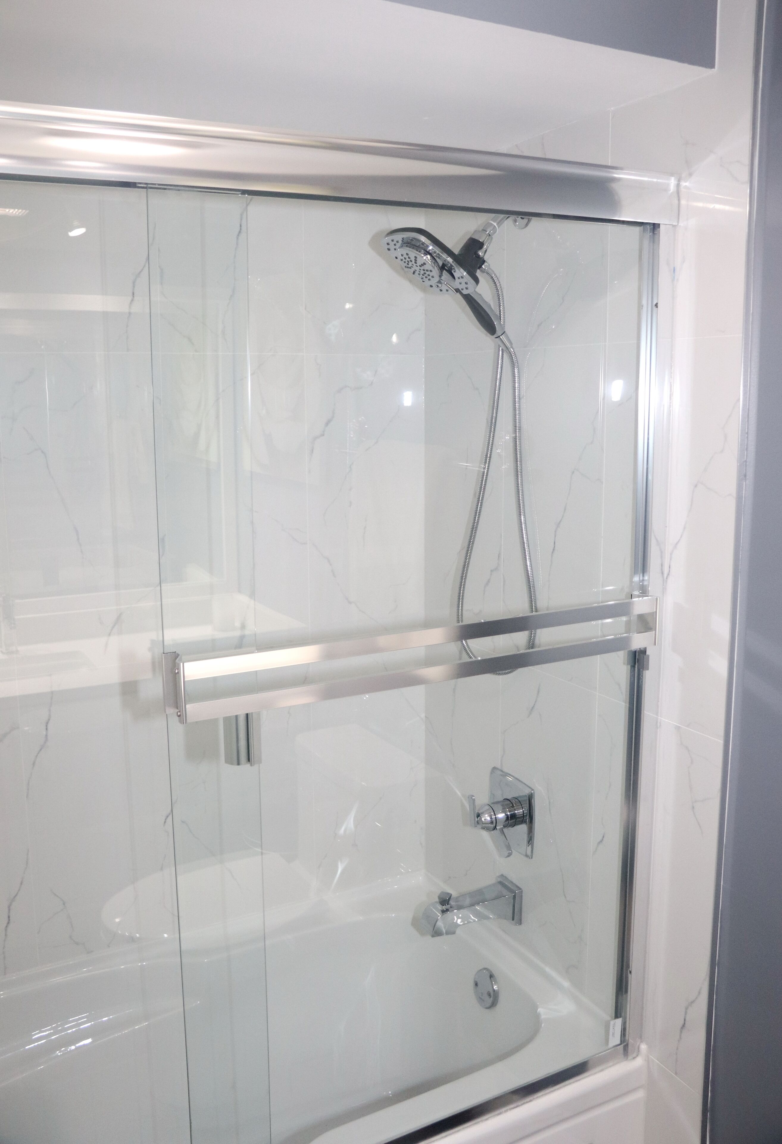 A glass-enclosed shower with a handheld showerhead and a handheld faucet.