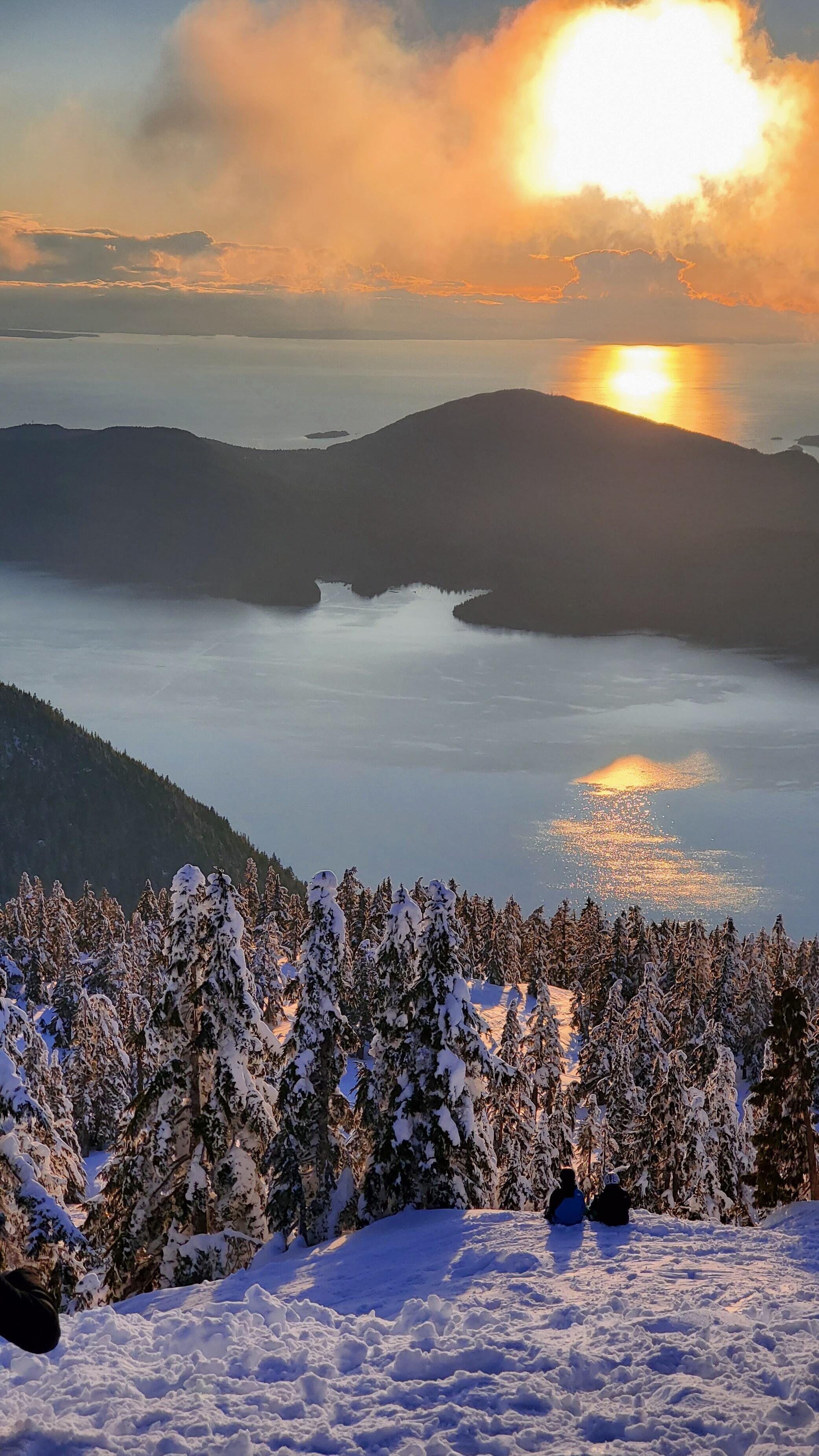Een besneeerd landschap met uitzicht op een meer en bergen tijdens de zonsondergang.