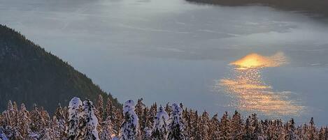 Een besneeerd landschap met uitzicht op een meer en bergen tijdens de zonsondergang.